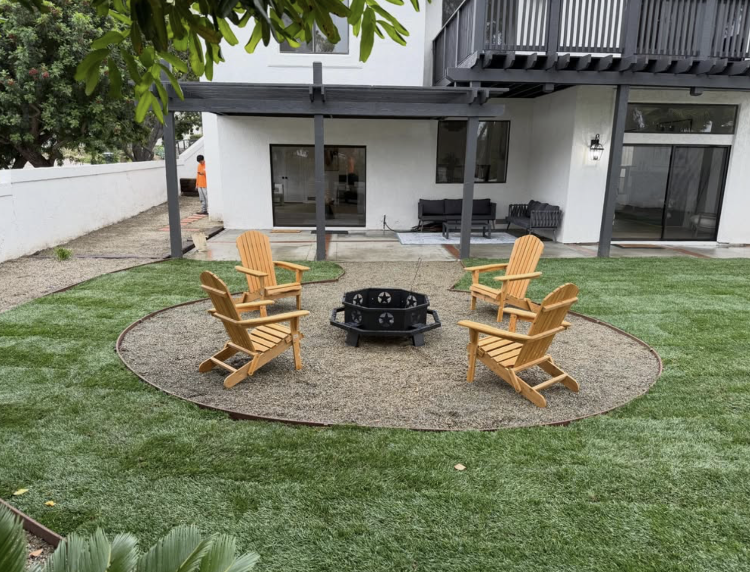 Backyard hardscape project with circular fire pit seating area, pergola, and lawn